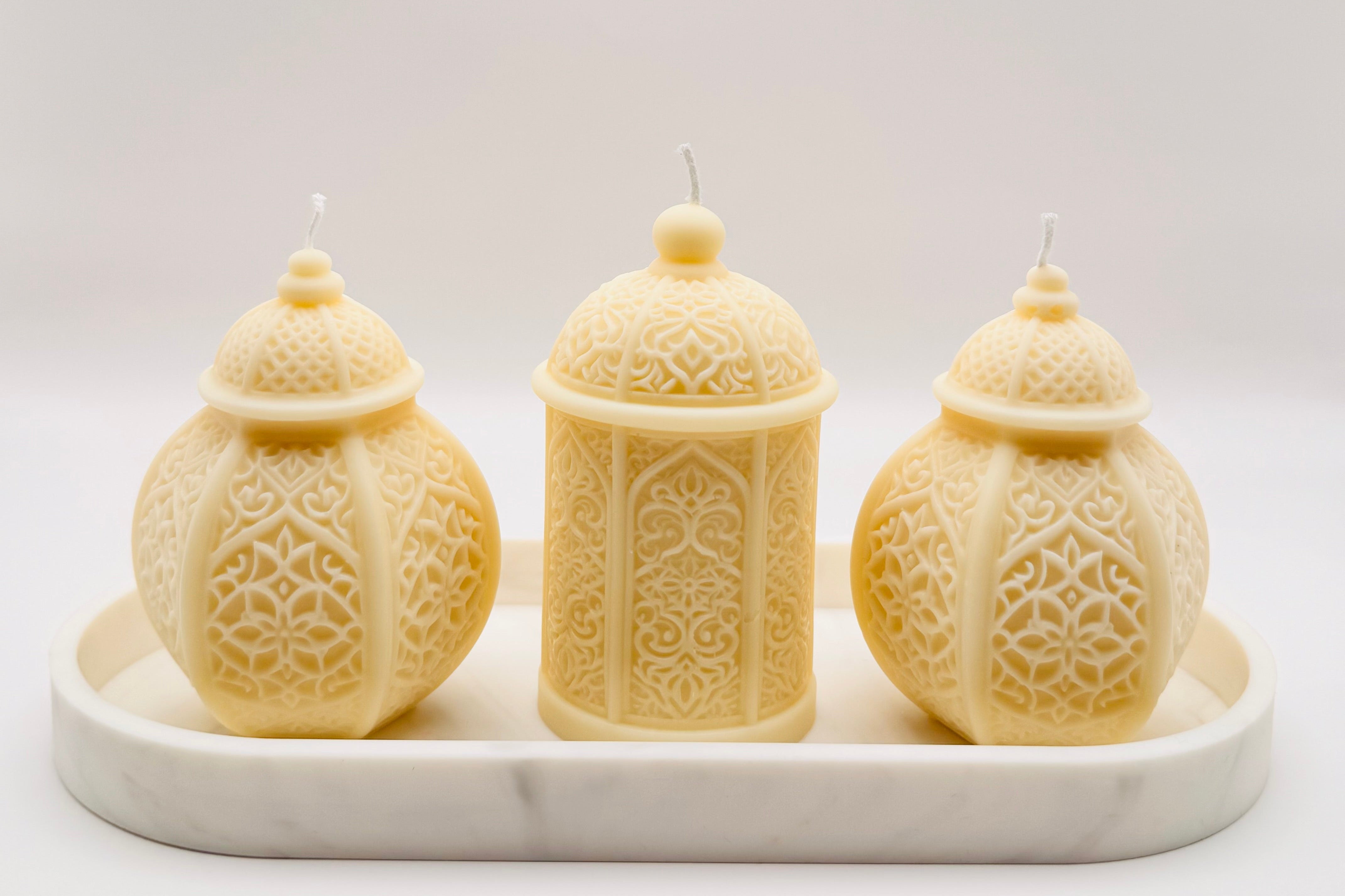 Three intricately designed candles on a white marble tray with a white background