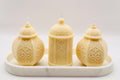Three intricately designed candles on a white marble tray with a white background
